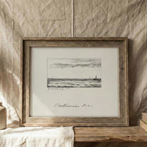 May include: A framed monochrome seascape print. The artwork shows a wavy ocean with sailboats under a cloudy sky. The frame is made of weathered wood, giving a rustic feel. The print is signed.