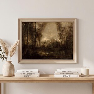 May include: A framed landscape painting in sepia tones depicting a dense forest and a calm body of water. The artwork is displayed in a light-colored wooden frame, showcasing a moody, atmospheric scene with dark trees and soft, diffused light.