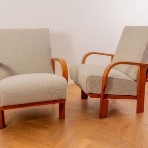 Può includere: Due poltrone vintage con rivestimento grigio chiaro e struttura in legno. Una sedia è in posizione verticale, l'altra reclinata. Le strutture in legno hanno una calda tonalità marrone-rossastra. Le sedie sono su un pavimento in legno.