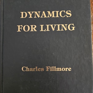 Pode incluir: Um livro de capa dura com o título "DYNAMICS FOR LIVING" de Charles Fillmore. O livro tem uma capa escura com letras douradas. O livro parece ser vintage ou antigo, com algum desgaste visível na capa.