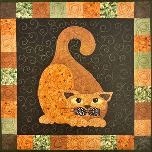 May include: A quilted square featuring a stylized orange cat with a black and white polka dot bow tie, set against a black background with swirling stitch details. The border is a patchwork of orange, green, and brown squares.