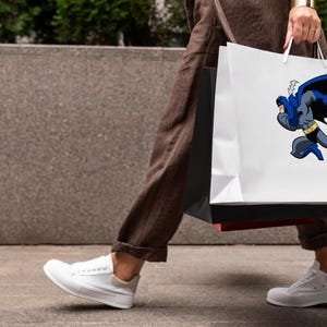 K&ouml;nnte beinhalten: Eine Person tr&auml;gt zwei Einkaufstaschen. Die Tasche rechts hat einen wei&szlig;en Hintergrund mit einem Comicbild von Batman in Blau und Schwarz. Die Tasche links ist schwarz.