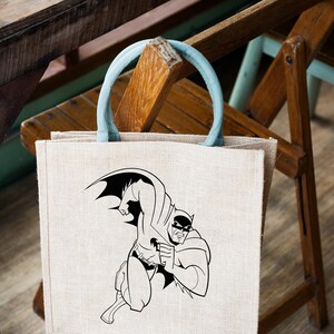 K&ouml;nnte beinhalten: Eine beige Jute-Tragetasche mit einem blauen Griff. Die Tasche zeigt eine Schwarzwei&szlig;-Illustration von Batman in einer Superheldenpose.