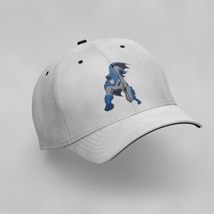K&ouml;nnte beinhalten: Wei&szlig;e Baseballkappe mit schwarzem Schirm und einem Comicbild von Batman in einem blau-grauen Kost&uuml;m.