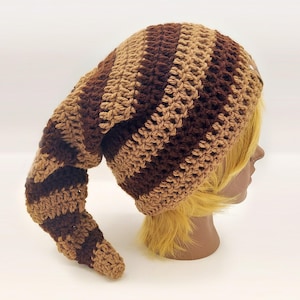 May include: A handmade crochet hat in shades of brown and tan. The hat features a long, pointed end and a striped pattern. The hat is designed to be worn on the head and is made of soft yarn.