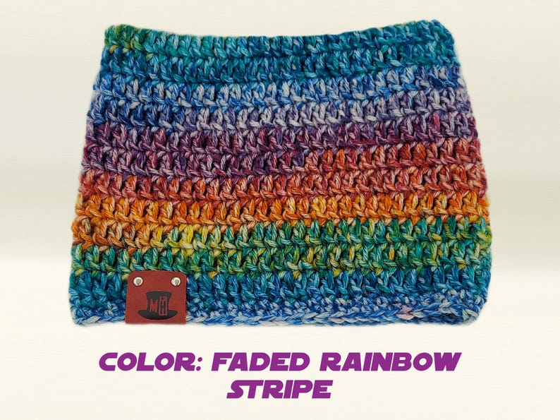 May include: A crocheted cowl in a faded rainbow stripe pattern. The cowl features a spectrum of colors, including blue, purple, orange, and green. A small brown leather tag with a logo is attached to the cowl. The text "COLOR: FADED RAINBOW STRIPE" is below the cowl.