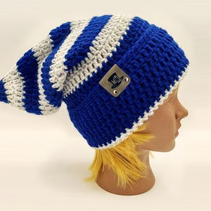 May include: A blue and white striped crochet beanie hat with a long, slouchy design. The hat features a small leather tag with a top hat logo. The hat is displayed on a mannequin head.