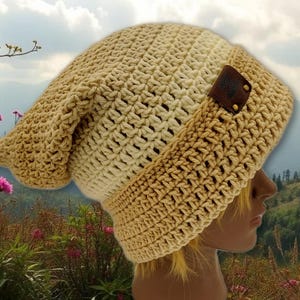 May include: A handmade, slouchy crochet beanie in shades of beige and tan. The hat features a wide, ribbed brim and a leather tag. The hat is made of a soft, textured yarn, perfect for cooler weather.