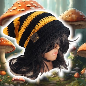 Puede incluir: Gorro de punto de crochet a rayas negras y amarillas con un borde de crochet negro. El gorro tiene un pequeño parche de cuero negro con un diseño.