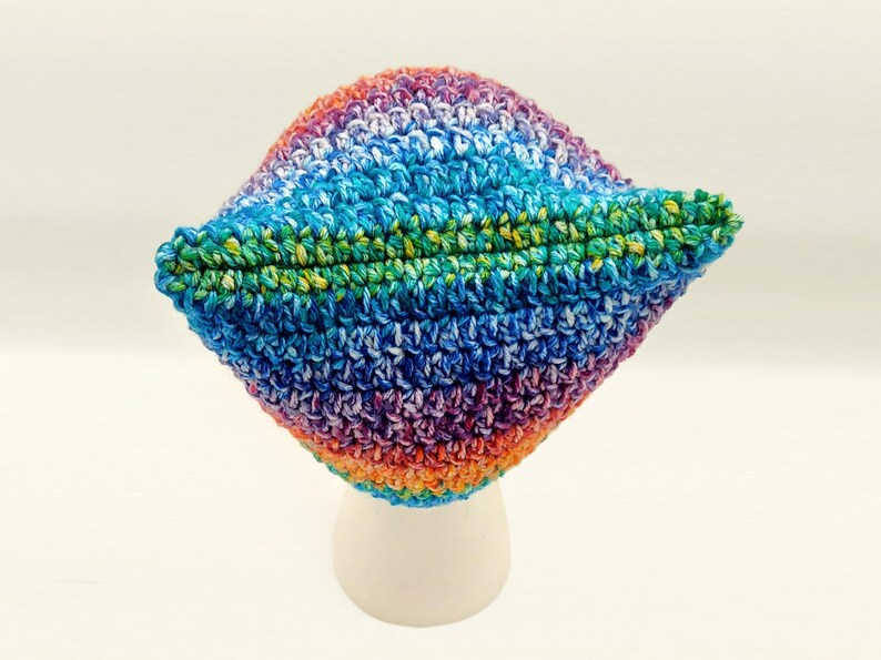 May include: A colorful, handmade crochet hat. The hat features a vibrant mix of colors, including blue, green, purple, orange, and white. The hat is displayed on a white stand against a white background. The hat's brim is folded up.