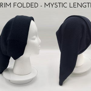 May include: A dark navy blue beanie with a folded brim and an elongated, drooping back section. The text BRIM FOLDED - MYSTIC LENGTH is displayed at the top. The hat features a textured, waffle-like knit pattern and is shown from two angles.