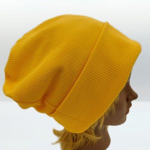 Puede incluir: Gorro de color amarillo mostaza con un patrón texturizado y acolchado. El gorro está doblado en el borde y tiene un ajuste holgado. El gorro está hecho de un material suave y flexible. El gorro se muestra en una cabeza de maniquí.