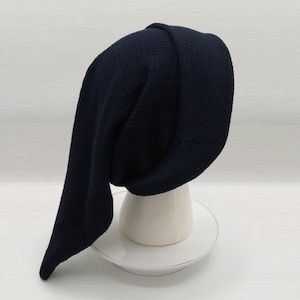 May include: A dark navy blue beanie with a textured, waffle-knit pattern. The hat features a long, slouchy design that hangs down on one side, with a wide, folded cuff at the base, displayed on a white mannequin head form.