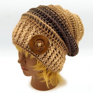 Pode incluir: Um gorro de crochê feito à mão em tons de castanho, bege e bronzeado. O chapéu apresenta um grande botão de madeira na lateral. O gorro é projetado com uma textura canelada e um ajuste folgado.