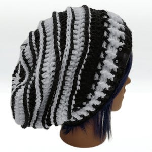 May include: A black and white striped crochet beanie hat. The hat is a slouchy style, with alternating vertical stripes of black and white. A small black tag is attached to the side of the hat.