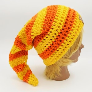 May include: A handmade, crochet hat in a vibrant combination of yellow and orange stripes. The hat features a long, pointed end, and a small, brown tag. The hat is designed to be worn on the head.