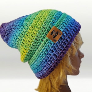 May include: A handmade, slouchy beanie in a vibrant rainbow of colors, including purple, blue, green, and yellow. The crochet hat features a brown leather tag with a top hat logo. This cozy hat is perfect for adding a pop of color to any outfit.