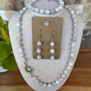 Puede incluir: Un conjunto de collar, pulsera y pendientes de piedras preciosas blancas. El collar y la pulsera están hechos de cuentas de piedras preciosas blancas facetadas. Los pendientes son de plata con gotas de piedras preciosas blancas.