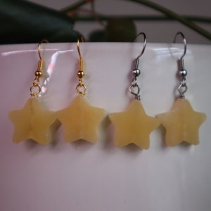 May include: A pair of star-shaped earrings with gold and silver hooks. The stars are a pale yellow color.