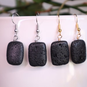 Op de afbeelding: Vier paar zwarte lavastenen oorbellen met verschillende gekleurde metalen haakjes. Twee paar hebben zilveren haakjes, één paar heeft een gouden haakje en één paar heeft een goudkleurig haakje.