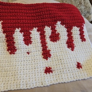 May include: A white crocheted square with red crocheted drips forming the word "drip" in the centre.