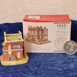 May include: A miniature replica of "The Gold Mining Stock Exchange" building, made of brick and stone, with a green roof. A box with a similar building illustration and a silver dollar coin are also present.