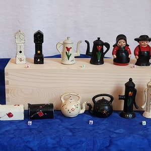 May include: A collection of cast iron figurines, including a clock, teapots, a Dutch couple, a mailbox, and a water pump. The figurines are painted in various colors, with floral and Dutch-themed designs. The water pump has the number "1965" on it.