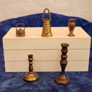 May include: A collection of five miniature brass objects including two candlesticks, a small lidded pot with a handle, a lantern-shaped item with a top loop, and a small vase. The items feature metallic gold and bronze tones with varied textures.