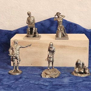 May include: Five pewter figurines on a wooden base. The figurines depict a man playing a musical instrument, a woman holding a hat, a man in a suit, a woman holding a wrench, and a man sitting with a dog.