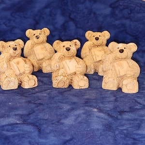 May include: Five small, brown, ceramic teddy bears are sitting on a blue fabric surface. Each bear is holding a book in its paws.