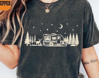 May include: Dark grey Comfort Colors t-shirt with a cream-colored graphic of a camper, trees, deer, stars, and a crescent moon. The shirt has the word "Pepper" on it.