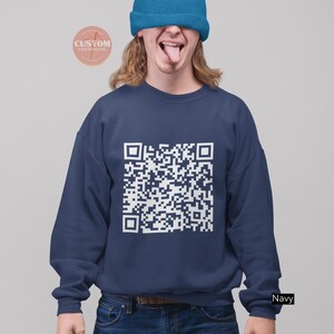 May include: A navy blue sweatshirt with a white QR code design. The model is wearing a blue beanie and has their tongue sticking out.