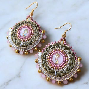 Può includere: Un paio di orecchini rotondi in perle rosa e verdi con dettagli dorati. Gli orecchini hanno un design intrecciato. Il centro di ogni orecchino presenta una pietra iridescente rosa e bianca.
