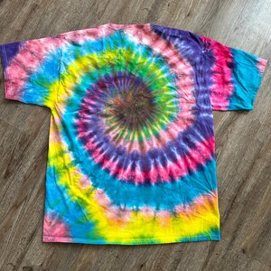 Puede incluir: Una camiseta tie-dye con un patr&oacute;n de espiral de rosa, azul, amarillo, verde y morado.
