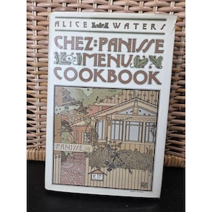 May include: A cookbook titled "Chez Panisse Menu Cookbook" by Alice Waters. The cover features an illustration of a building with the restaurant's name. The title is in brown and green, with a white background.