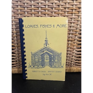 May include: A spiral-bound booklet with a yellow cover featuring a blue illustration of a church. The text "LOAVES, FISHES & MORE" is at the top, with "ABBOTT'S CREEK BAPTIST CHURCH" and location details below.