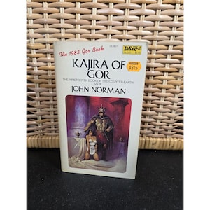 May include: A paperback book titled "Kajira of Gor" by John Norman. The cover features a fantasy illustration of a man and woman. The book is from 1983 and includes the text "The Nineteenth Book of the Counter-Earth Saga."