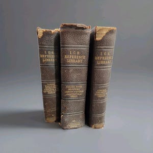 May include: Three vintage brown leather-bound books with gold lettering. The spines read "I.C.S. REFERENCE LIBRARY" and include titles like "CARPET, WALLPAPER, BOOKCOVER, LINOLEUM & ARCHITECTURAL DESIGN". The books are slightly worn, suggesting age.