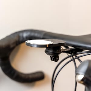 Op de afbeelding: Een zwart stuur van een fiets met een zwarte en zilveren houder voor een camera of telefoon.