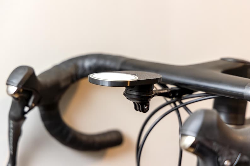 Op de afbeelding: Een zwart stuur van een fiets met een zwarte en zilveren houder voor een camera of telefoon.