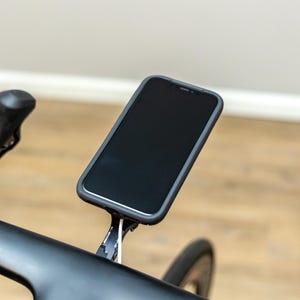 Op de afbeelding: Een zwarte smartphone gemonteerd op een zwart stuur van een fiets met een witte kabel.