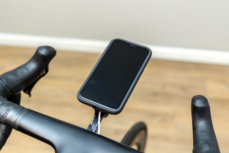 Op de afbeelding: Een zwarte smartphone gemonteerd op een zwart stuur van een fiets met een witte kabel.