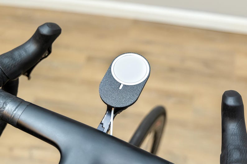 Op de afbeelding: Een zwart stuur van een fiets met een zwart-witte telefoonhouder die in het midden is bevestigd.