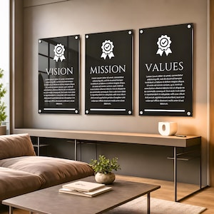 May include: Three rectangular black acrylic wall signs mounted with silver standoffs. Each sign features a white ribbon icon with a checkmark, the headings VISION, MISSION, and VALUES, and placeholder text in white, sans-serif font.