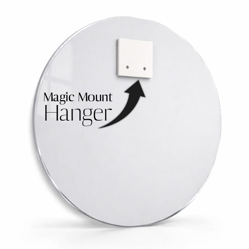 May include: A circular, clear acrylic panel featuring a white square mounting bracket attached to the upper centre. The text Magic Mount Hanger is printed in black, accompanied by a black arrow pointing towards the mounting bracket.