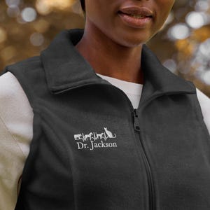 May include: Black fleece vest with a zipper closure and a white embroidered design of a line of animals and the text "Dr. Jackson".