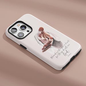May include: White phone case featuring a watercolor illustration of a hand reaching out. The case has a black camera lens frame and the text "Blessed are the pure in heart for they shall see God."