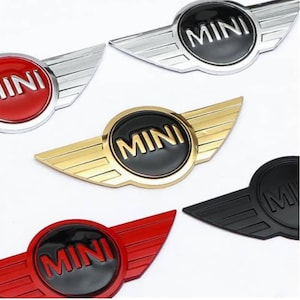 May include: Five different car emblems with the word "MINI" in black lettering on a white background. The emblems are in different colours: silver, gold, red, black, and a combination of red and black.