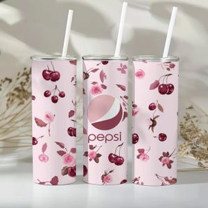 May include: Three pink and white stainless steel tumblers with a cherry and floral pattern. The tumblers have lids and straws. The middle tumbler has the Pepsi logo on it.