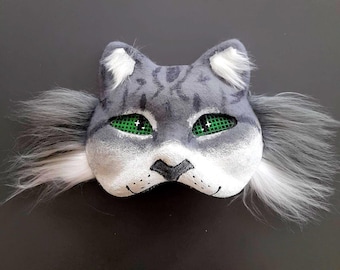 May include: A gray and white cat mask with green eyes and white fur around the edges.
